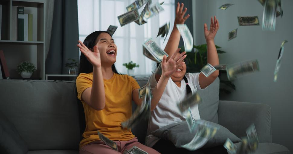 Free Image of Portrait of a young woman and teenage girl enjoying scattering cash bills on a sofa in the living room at home. 