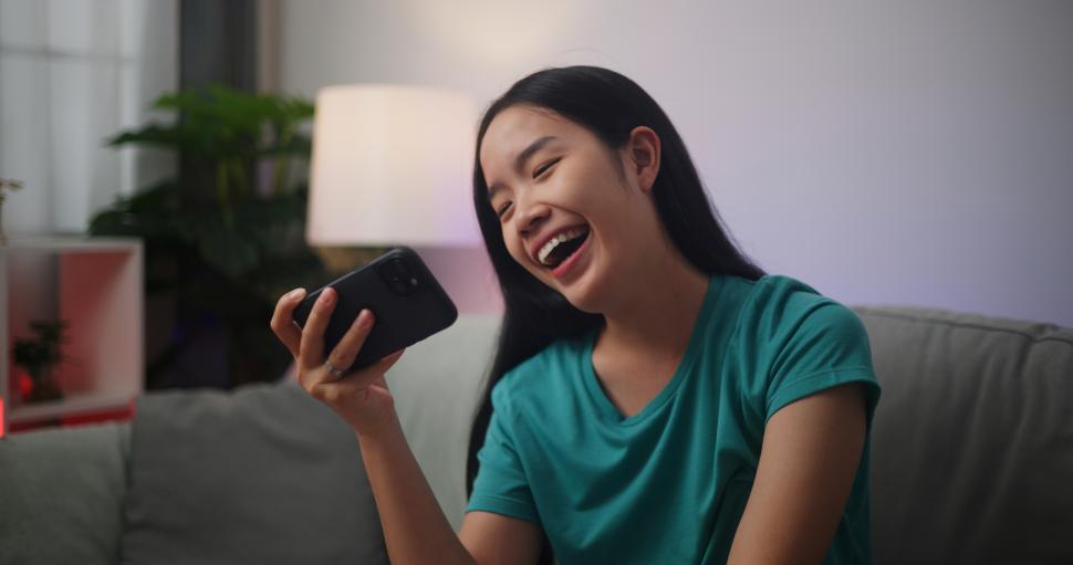 Free Image of Portrait of Young Asian woman enjoys playing online esport games on smartphone sitting on sofa in the living room at home,Gamer lifestyle concept. 