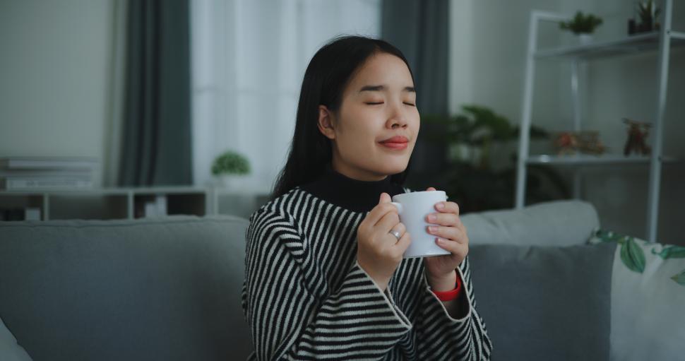 Free Image of Portrait of Relaxing young woman holding cup enjoy smell coffee or tea and drinking with happiness in morning while sit on sofa in living room,Free time,take break in home,smiling 