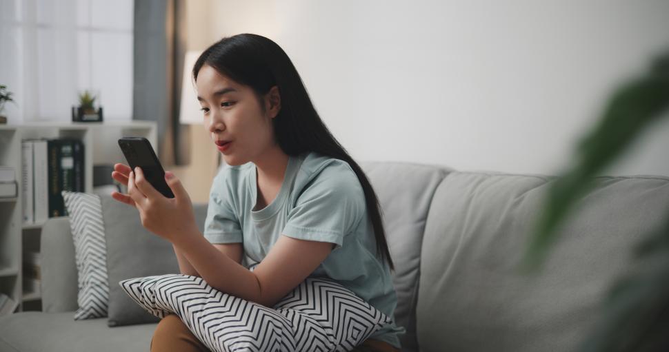 Free Image of Selective focus, Happy young woman sitting on sofa look in mobile phone 