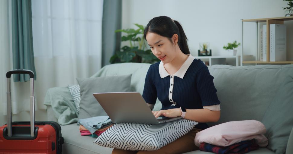 Free Image of Portrait of Asian teenager woman sitting on sofa using laptop for prepare booking hotel and airplane tickets 