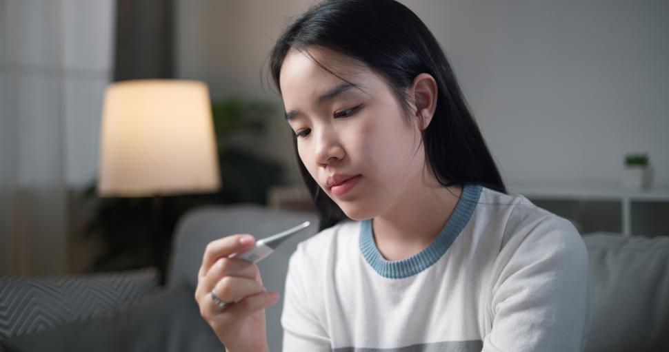 Free Image of Portrait of Unwell young woman have a fever and measure temperature with a thermometer while sitting on sofa in the living room at home, healthcare woes 