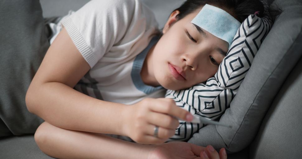 Free Image of Portrait of Unwell young woman have a fever and measure temperature with a thermometer while lying on sofa in the living room at home, healthcare woes 