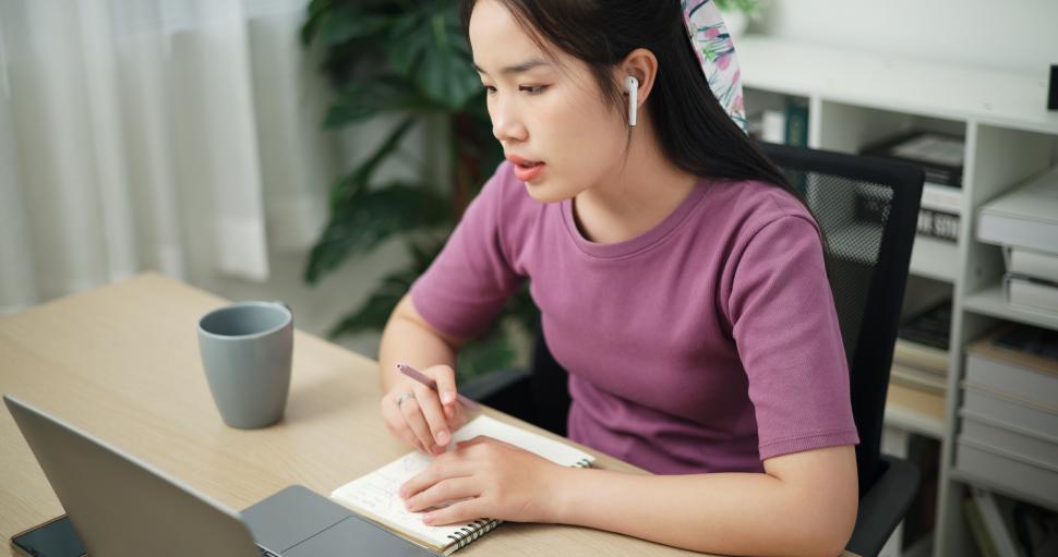 Free Image of High angle view, Young asian businesswoman wear wireless headphones having a video conference on laptop and writing on note at home office, online meeting for remote work 