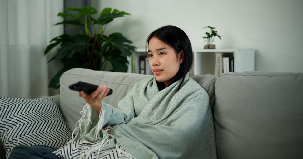 Free Image of Portrait of Relaxed young Asian woman sitting covered in a cloth and watches television on the sofa in the living room at morning ,Free time 