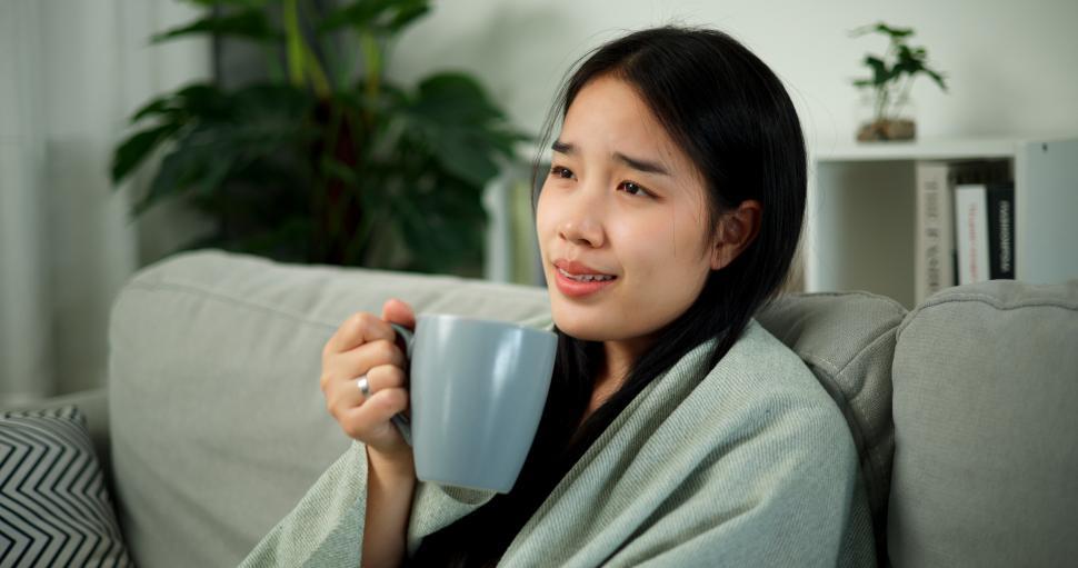Free Image of Portrait of Relaxed Asian woman sipping coffee while watching television on the living room sofa in the morning. Free time. 
