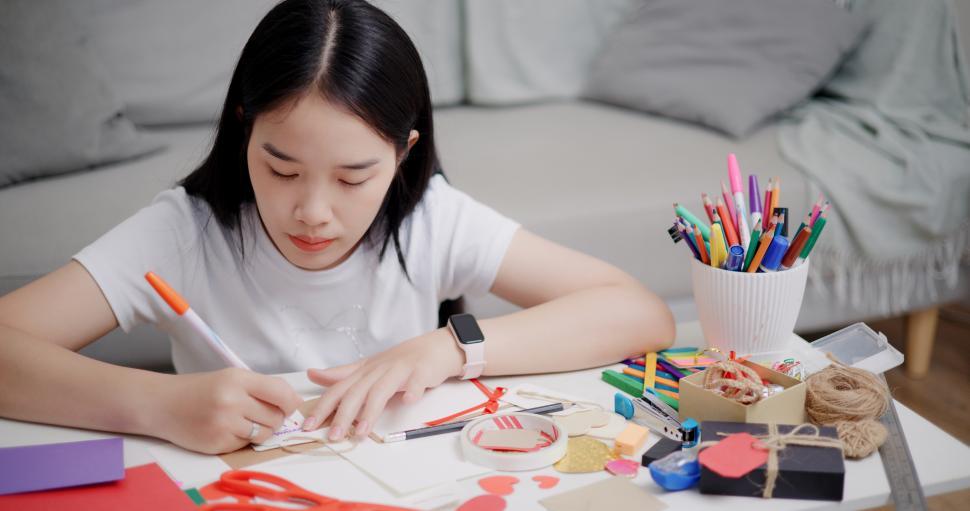Free Image of High angle view, Young Asian woman sitting on the floor writing a message on a greeting card. Holiday hobbies, crafts, DIY cards. 