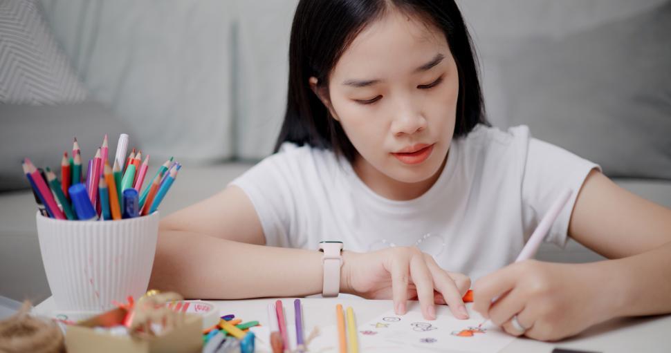 Free Image of High angle view, Young Asian woman sitting on the floor coloring a greeting card in the living room, Holiday hobbies, crafts, DIY cards 
