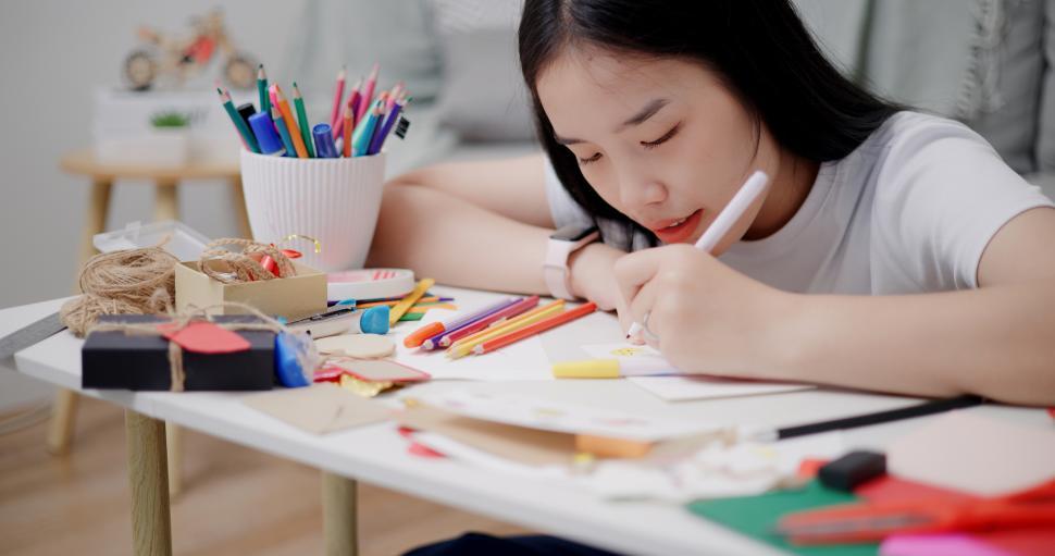 Free Image of Selective focus, Young Asian woman sitting on the floor coloring a greeting card in the living room, Holiday hobbies, crafts, DIY cards 