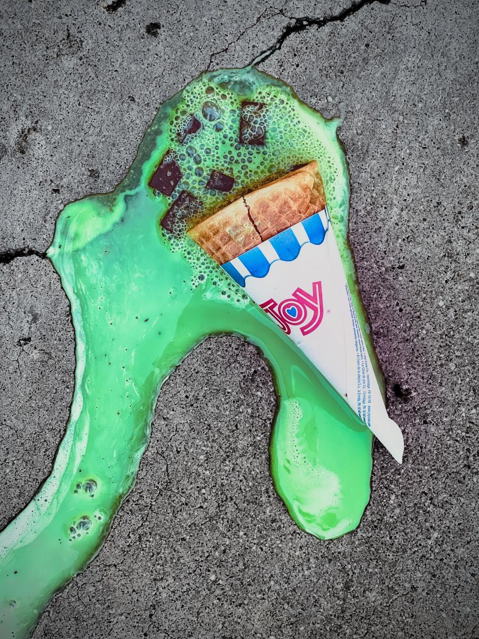 Free Image of Melting ice cream cone spills vibrant green mint  chocolate chip on concrete surface during summer afternoon 