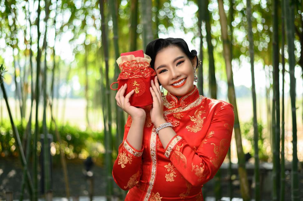 Free Image of Asian pretty Chinese woman in cheongsam holding envelopen inside a Red amulet bag 