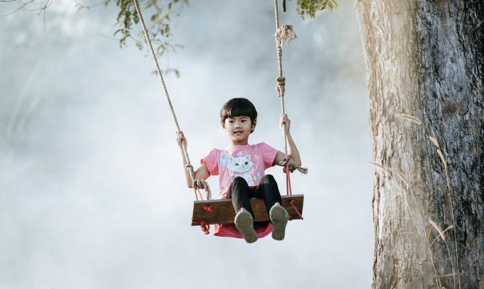 Free Image of Asian cute girl joyful on rope swing under tree 