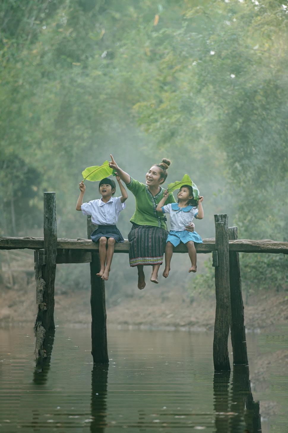 Free Image of Young mother enjoying time with two daughters on wooden bridge 