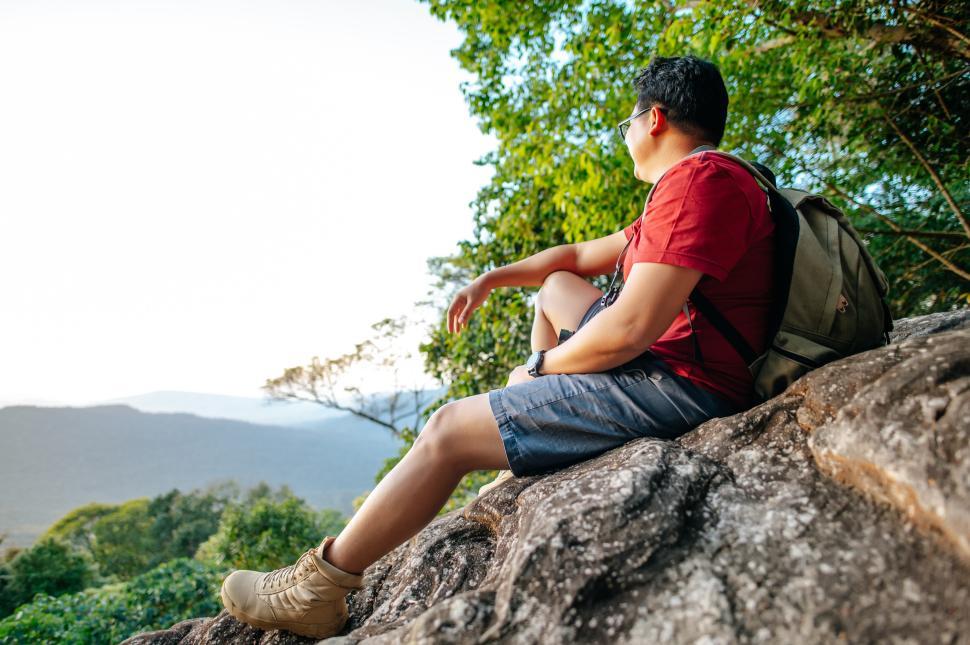 Free Image of Young backpacker man sitting on rocky cliffs with backpack 