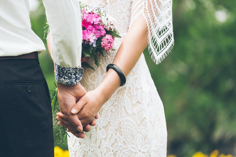 Free Image of Bride and groom holding hands with wedding bouquet visible 