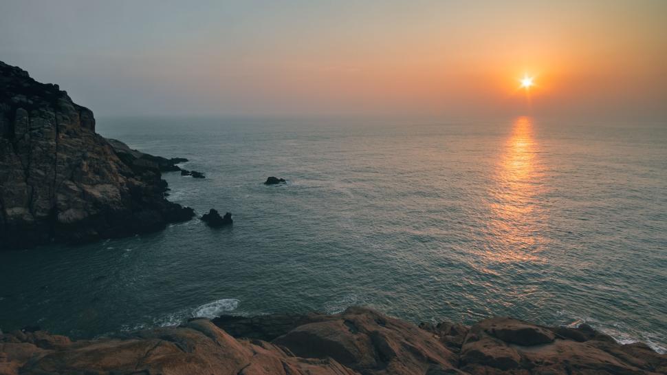 Free Image of Sunset view over the ocean with cliffs in the foreground 