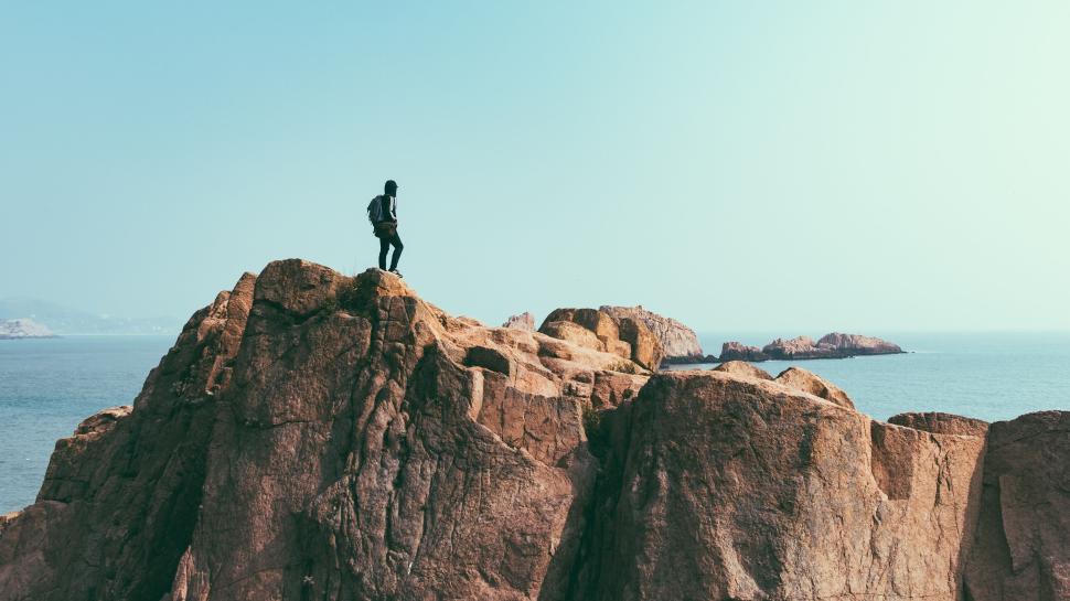 Free Image of Solo hiker on rocky cliff overlooking expansive ocean view 