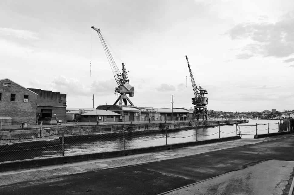 Free Image of Industrial cranes over calm river with overcast sky. 