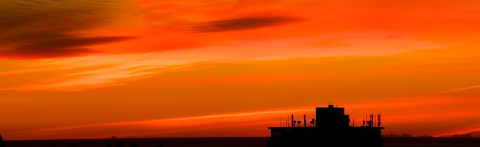 Free Image of Silhouette of building rooftop against bold orange sky. 