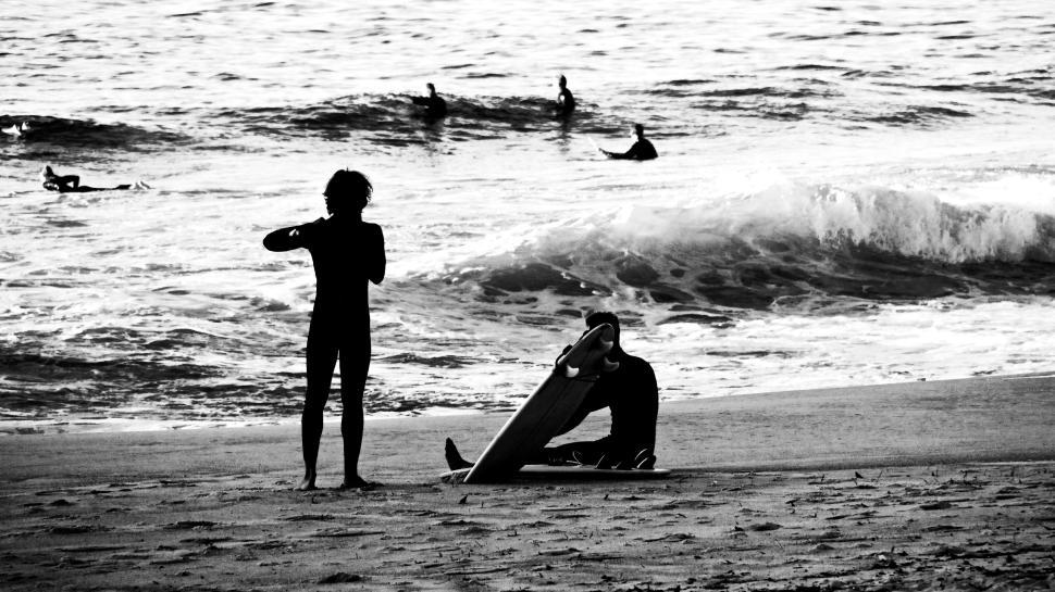 Free Image of Surfers prepare to catch waves sitting on beach sand. 