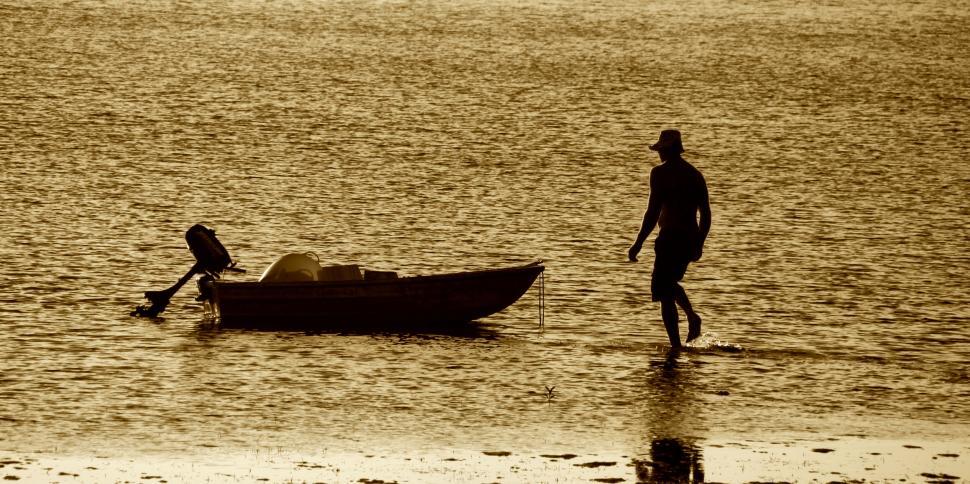 Free Image of A man wading with a small boat during golden hour 
