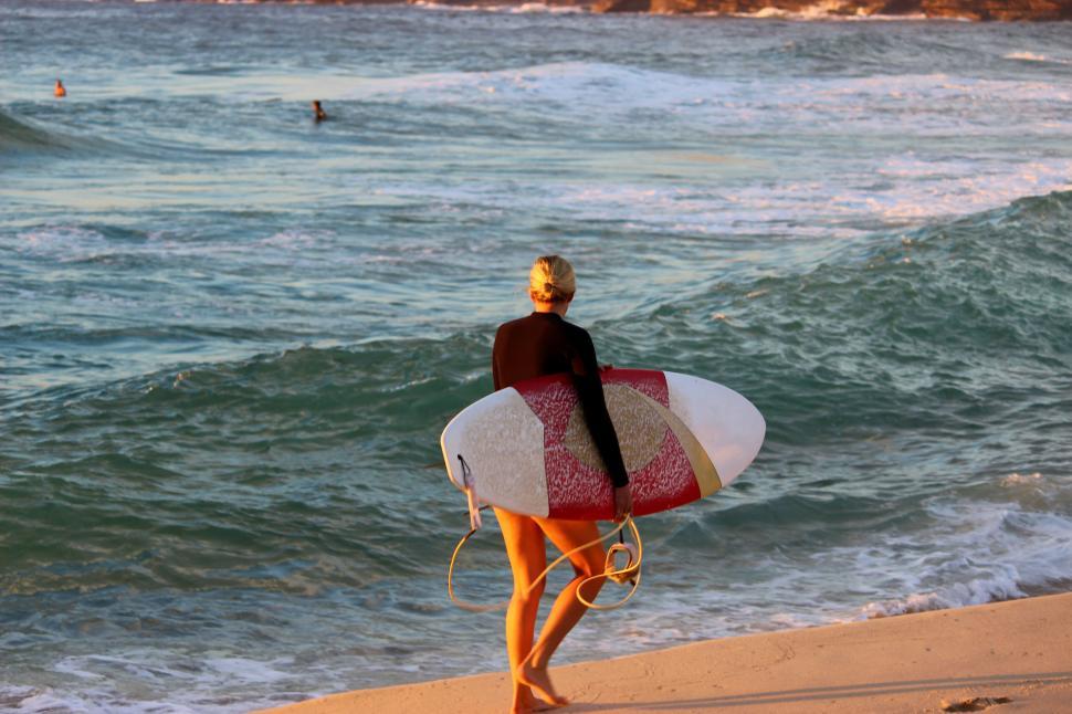 Free Image of Surfer girl at beach, holding board, wavy ocean backdrop. 