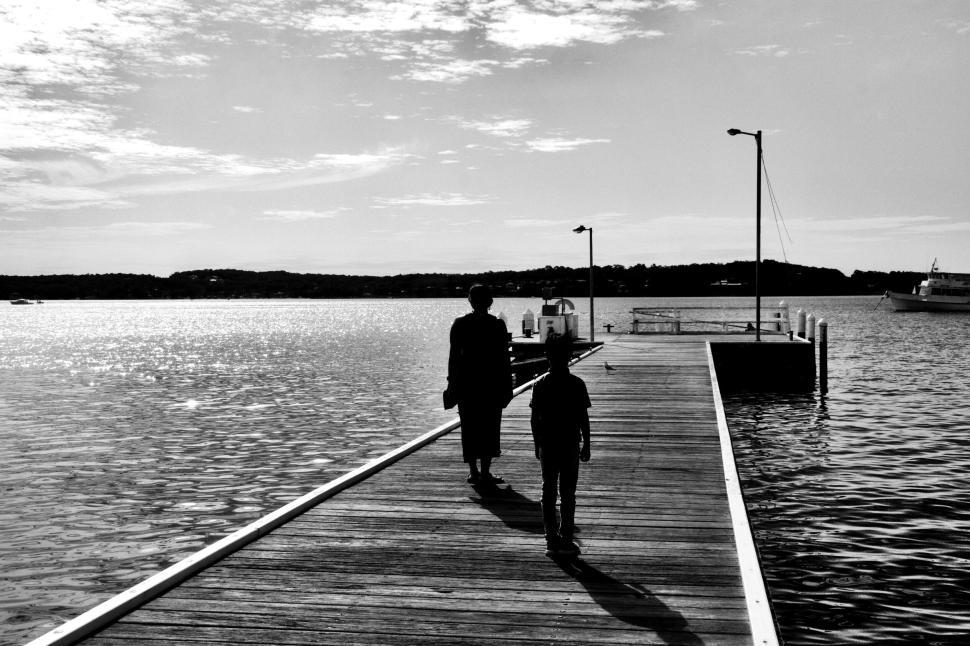 Free Image of Black and white image of two people walking on dock. 