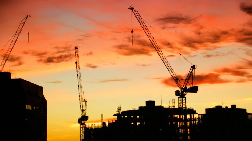 Free Image of Construction cranes silhouetted against a sunset sky. 