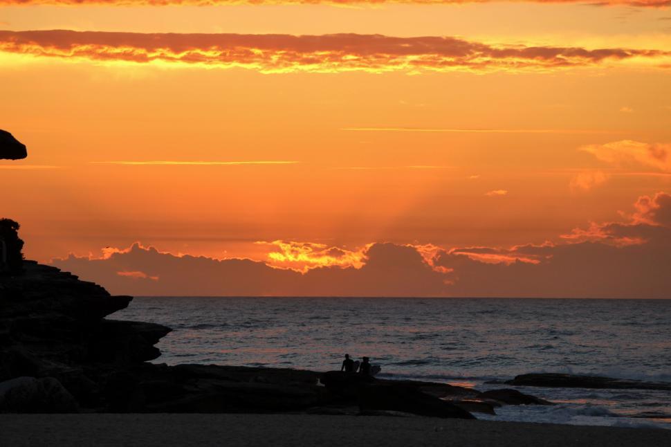 Free Image of Silhouetted figures on a rocky shore at sunset time. 