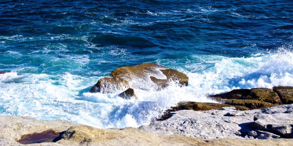 Free Image of Waves crashing onto rocky shoreline with deep blue hues 