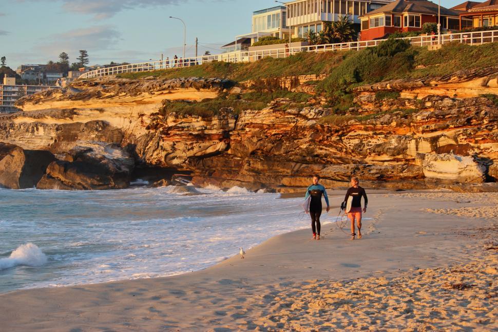 Free Image of Two people walking along a picturesque coastal beach. 