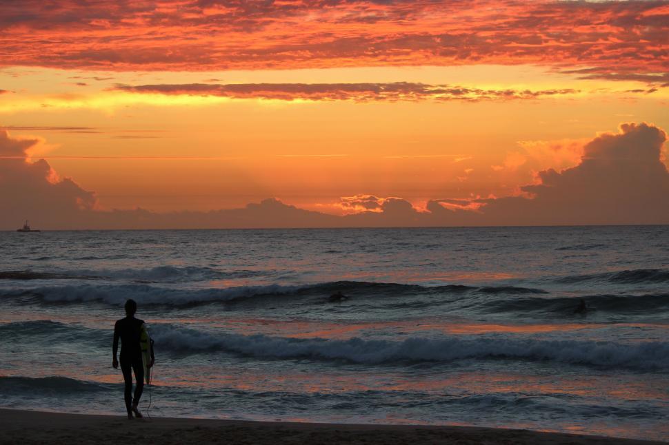 Free Image of Beach sunset with silhouetted figure holding surfboard. 
