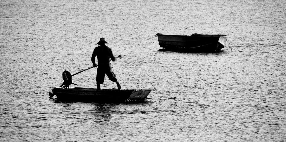 Free Image of Man rowing boat on a peaceful lake in black and white. 