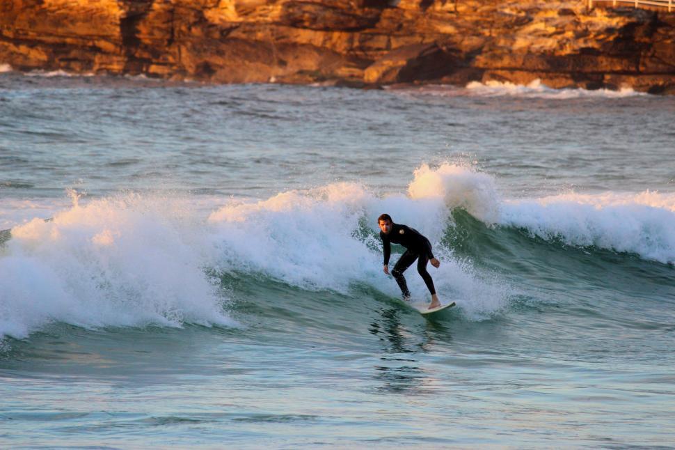Free Image of Surfer riding a wave at sunset near rocky coastline. 