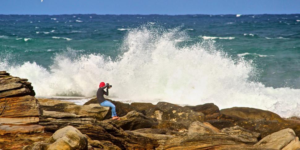 Free Image of Photographer capturing ocean waves from rocky shore. 
