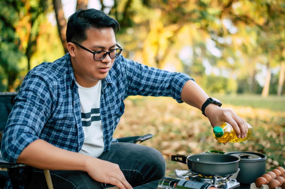 Free Image of Portrait Thai traveler man glasses pouring sunflower oil into a frying pan 