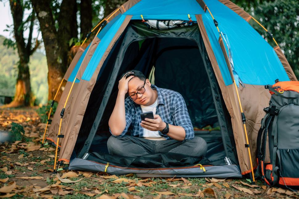 Free Image of Portrait of Asian traveler man glasses using smartphone in tent camping 