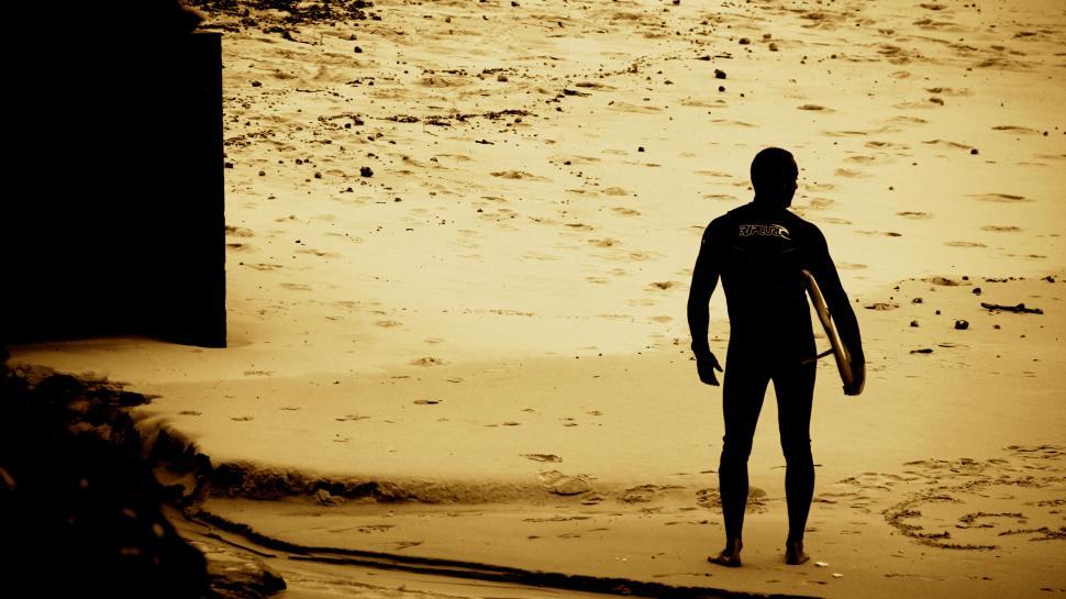 Free Image of Man with surfboard stands on sandy beach looking at ocean 