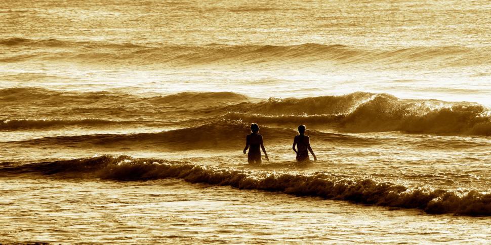 Free Image of Two people standing in ocean waves during sunset time 
