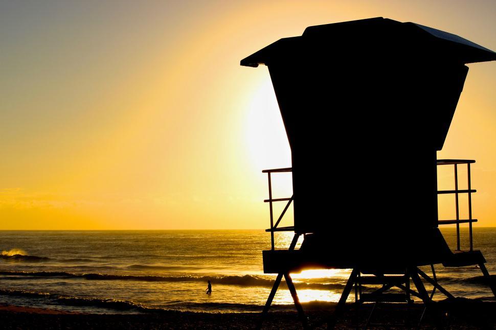 Free Image of Lifeguard tower silhouetted against a golden sunset sky 