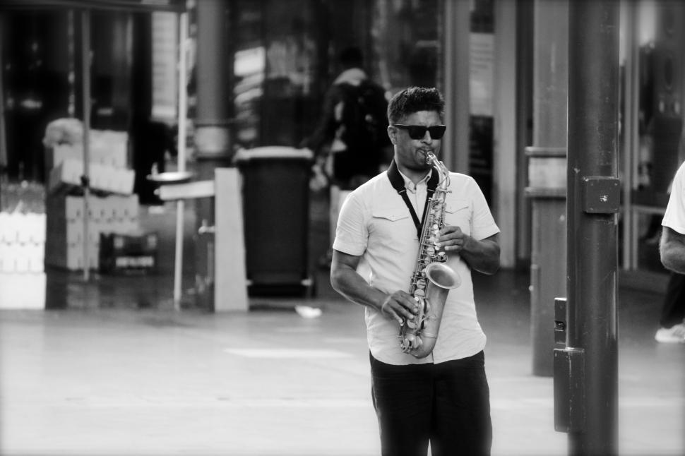 Free Image of Man playing saxophone on street wearing sunglasses. 