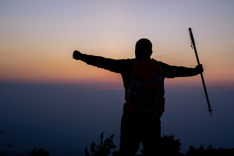 Free Image of Silhouette of cheering hiking man open arms to the sunrise stand on mountain 