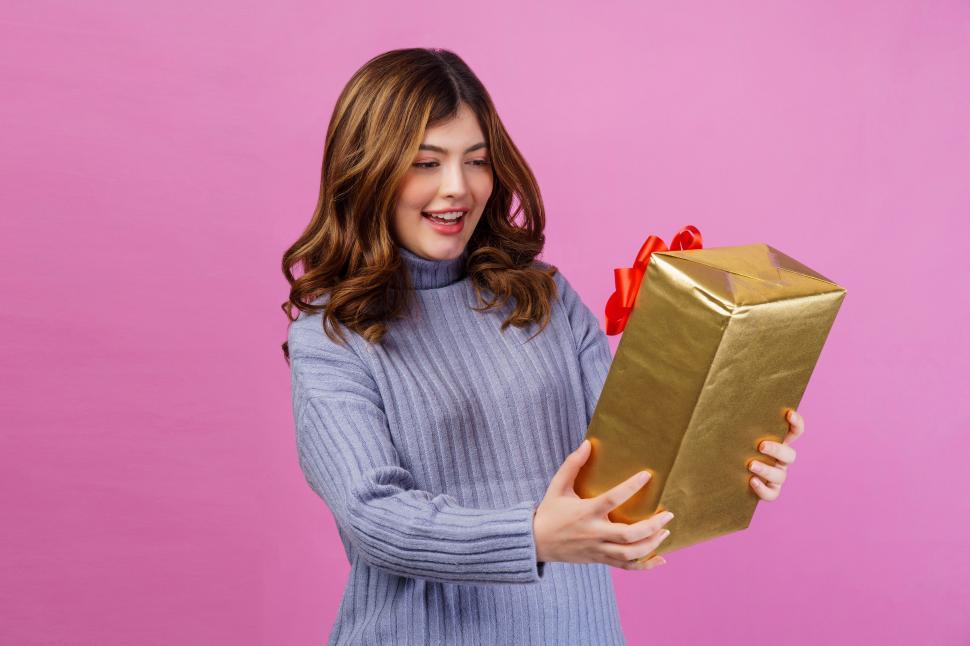 Free Image of Portrait of Excited surprised young woman holding gift in her hands isolated over pink background 
