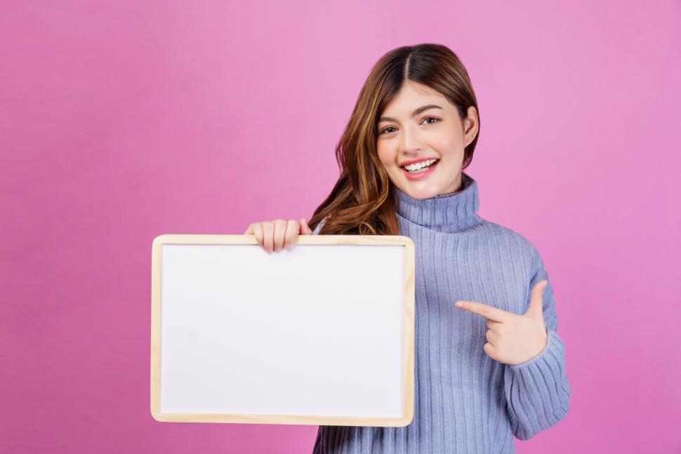 Free Image of Portrait of Happy young woman holding an empty white placard over isolated pink background. 