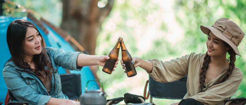 Free Image of Young women cheer and drink beverage  front of camping tent 