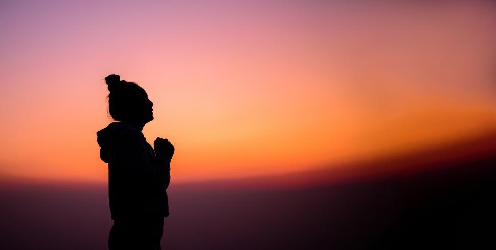 Free Image of Silhouette of Side view portrait of a woman praying and looking above at sunset 