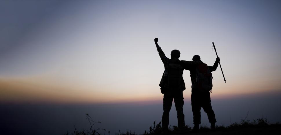 Free Image of Silhouette of cheering hiking men open arms to the sunrise stand on mountain 