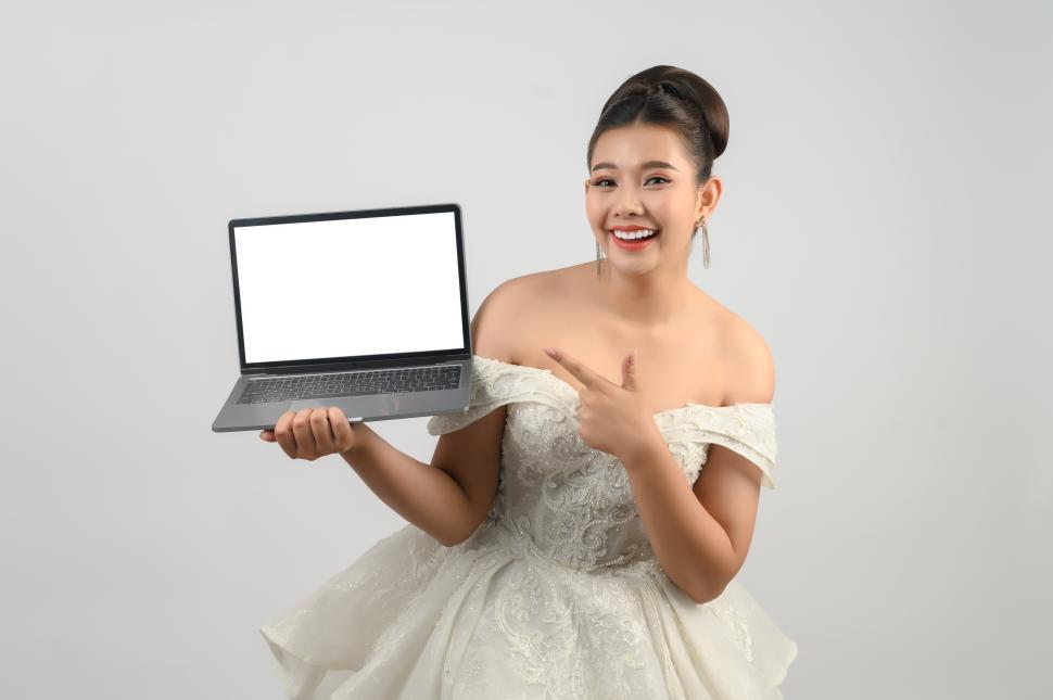 Free Image of Young asian beautiful bride pose with mockup laptop computer in hand 
