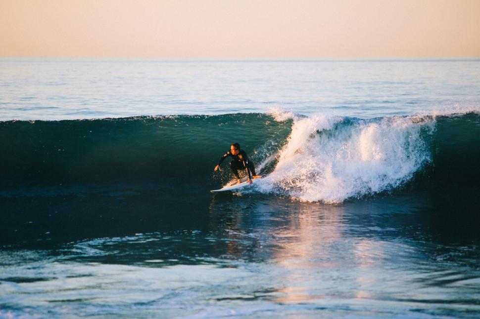 Free Image of Surfer rides a wave at sunset on a calm ocean 