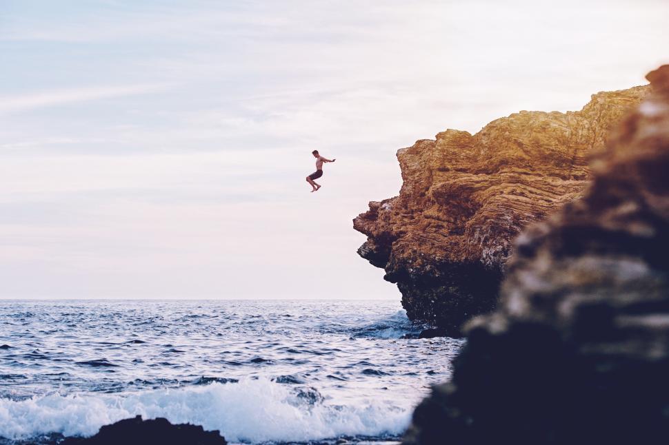 Free Image of Person jumping off a cliff into the ocean at sunset 